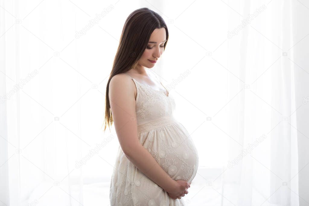 pregnancy and motherhood concept - portrait of happy beautiful pregnant woman posing over window