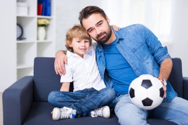 Genç baba ve oğul futbol topuyla kanepede oturuyorlar.