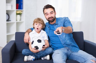 Genç baba ve oğul televizyonda futbol izliyorlar.