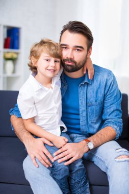 Küçük baba ve oğlu evdeki kanepede oturuyor.
