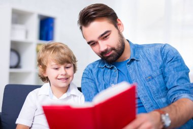 Aile kavramı. Genç baba ve küçük oğlu evde birlikte kitap okuyorlar.