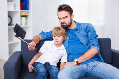 Aile kavramı - komik genç baba ve küçük oğlu evde akıllı telefonla selfie çekiyorlar.