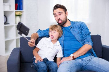 Aile kavramı - komik genç baba ve küçük oğlu akıllı telefonla selfie çekiyorlar.