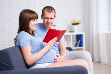 Genç hamile çift modern oturma odasında kitap okuyor.