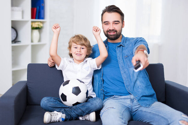 счастливый молодой отец и сын смотрят футбол по телевизору

