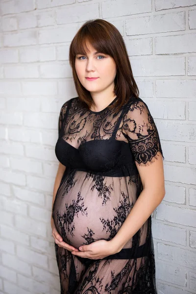 妊娠中の女性が白いレンガの壁の背景に腹を触れ — ストック写真