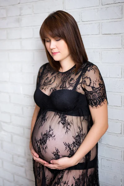 妊娠と産前のコンセプト 白いレンガの壁の上に彼女の腹に触れる妊婦の肖像 — ストック写真