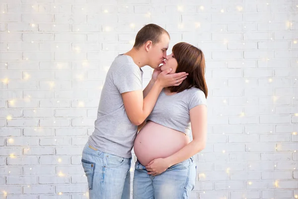 Portrait Happy Pregnant Couple Kissing White Brick Wall Christmas Lights — Stock Photo, Image