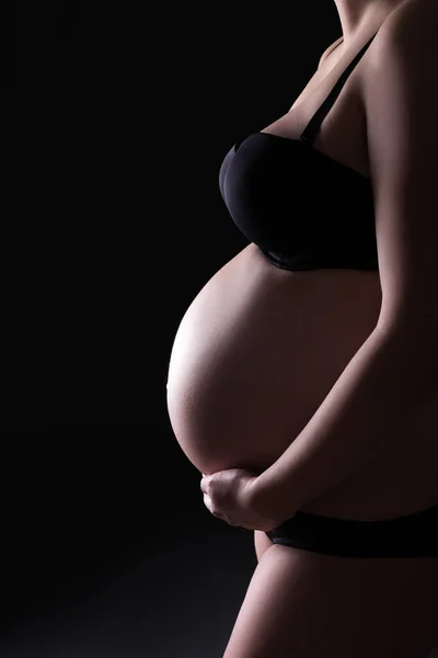 妊娠中のお腹を黒い背景で塞いで — ストック写真
