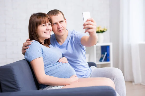 Mutlu Hamile Kadın Kocası Modern Oturma Odasında Akıllı Telefonlarıyla Selfie — Stok fotoğraf