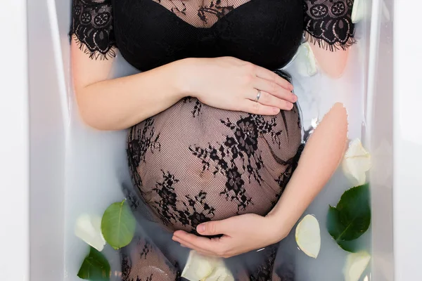 黒いレースのドレスを着た妊婦がミルクと花びらでお風呂でリラックスして — ストック写真