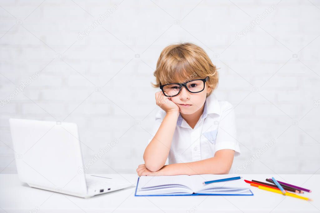 bored little school boy in glasses doing homework at home