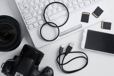 Kamera, lensler, fotoğrafçılık ekipmanları, akıllı telefon ve dizüstü bilgisayarın beyaz arkaplan üzerindeki üst görünümü