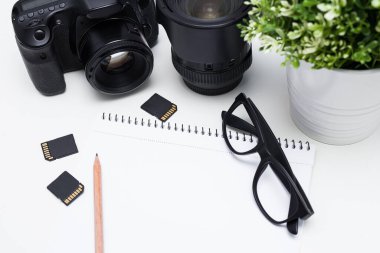 Fotoğrafçının iş yerinin üst görüntüsü - kamera, fotoğraf ekipmanı, not defteri ve gözlük beyaz masa arkaplanı üzerinde