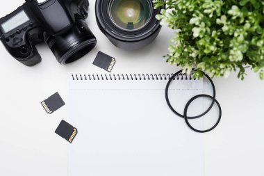 Fotoğrafçının iş yerinin üst görüntüsü - kamera, fotoğrafçılık ekipmanı ve beyaz masa arkaplanı üzerindeki not defteri
