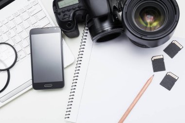 Fotoğrafçının iş yeri - kamera, fotoğraf makinesi, dizüstü bilgisayar, akıllı telefon ve beyaz masanın üzerinde kalem olan not defteri
