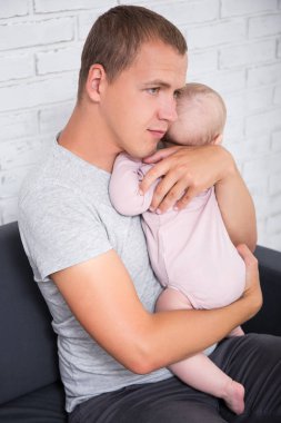 Evde kucağında küçük bir kızı tutan genç babanın portresi.