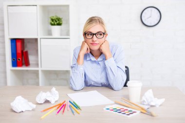 Yaratıcılık, fikir ve ilham konsepti - boya fırçaları, renkli kalemler ve buruşuk kağıtlarla yeni fikirleri düşünen yorgun genç kadın tasarımcı