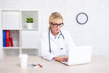 Modern ofiste oturan ve dizüstü bilgisayar kullanan kadın doktorun portresi.