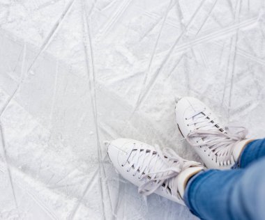 Yeni deri patenlerle bacakların üst görüntüsünü kapat ve buz pistindeki beyaz çizikli buzun üzerine alanı kopyala
