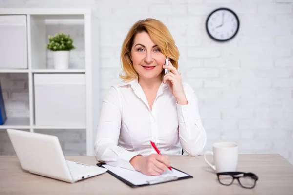 Vrolijk Volwassen Zakenvrouw Zitten Modern Kantoor Praten Telefoon Schrijven Iets — Stockfoto