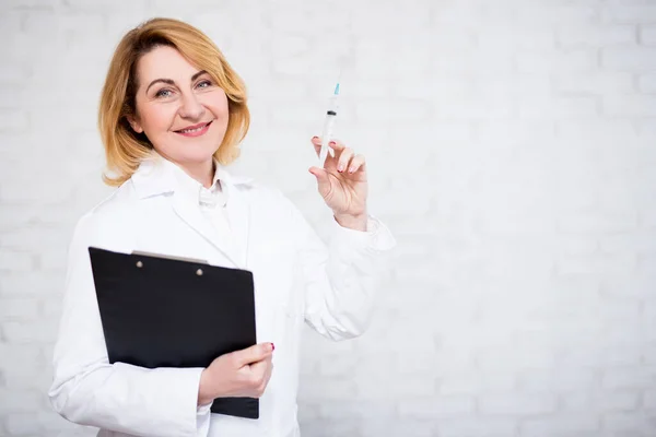 ヘルスケア 予防接種 美容の概念 成熟した女性医師は白いレンガの壁に注射器とクリップボードを保持 — ストック写真