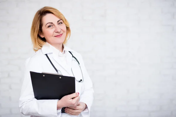 Retrato Doctora Madura Enfermera Sujetando Portapapeles Sobre Pared Ladrillo Blanco — Foto de Stock