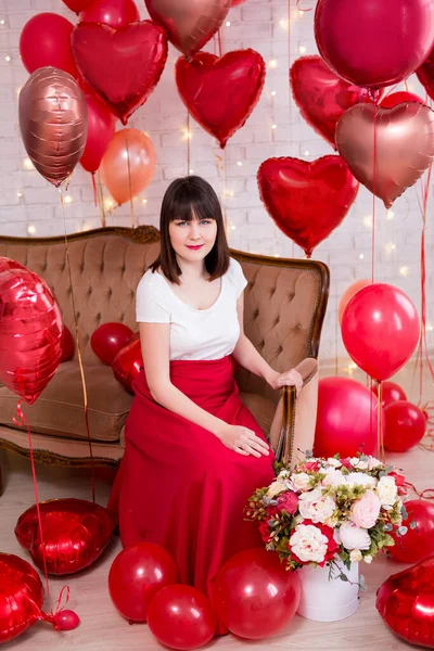 情人节的概念 坐在老式沙发上的年轻女子的全长肖像 上面有红色心形氦气气球 — 图库照片