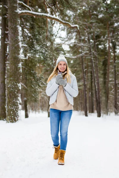 full length portrait of young blond woman walking in winter forest with thermo cup of coffee