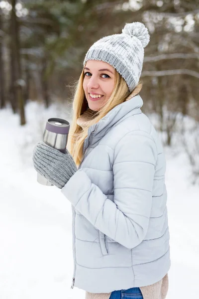 在冬季公园或森林里喝热咖啡或茶的金发年轻女子 — 图库照片