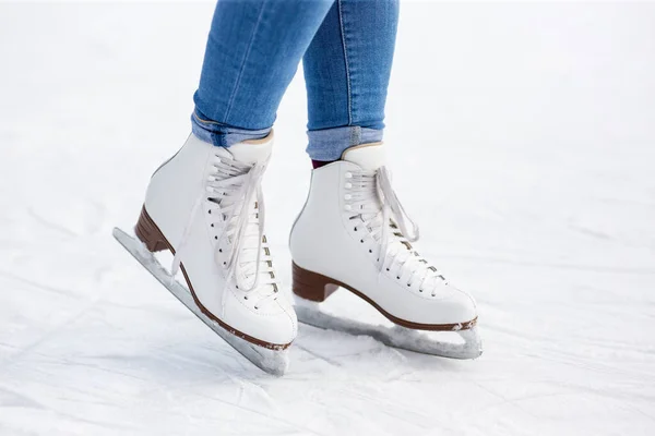 close up of female legs in leather skates over white ice at rink