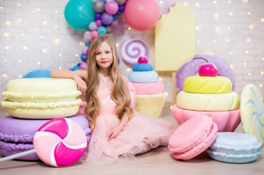 Büyük yapay şekerlerle oturan küçük tatlı bir kızın portresi.