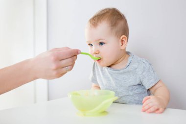 Plastik kaşıktan yemek yiyen küçük tatlı bir kızın portresi.