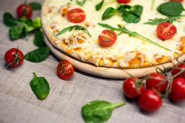 Domatesli ve otlu vejetaryen pizzayı ahşap arka planda kapat.