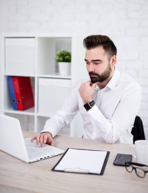 Genç yakışıklı sakallı iş adamı ofiste bilgisayar kullanıyor.