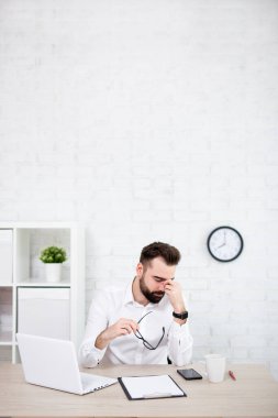 Stres ya da baş ağrısı - ofiste oturan yorgun işadamının portresi - beyaz tuğla duvarın üzerine kopyalama alanı