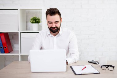 Modern ofiste dizüstü bilgisayar kullanan neşeli sakallı iş adamının portresi.