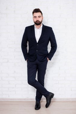 Genç sakallı iş adamının beyaz tuğla duvarın arkasındaki portresi.