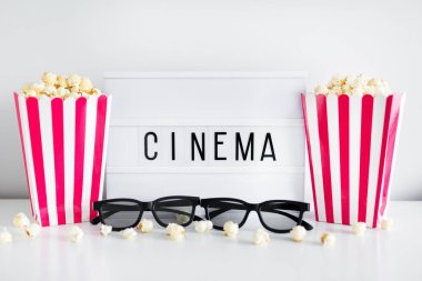 Sinema konsepti - patlamış mısırlı kırmızı çizgili kutular, 3 boyutlu gözlük ve sinema kelimeli ışık kutusu