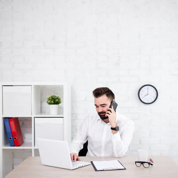 Yakışıklı Sakallı Adamı Ofiste Bilgisayar Kullanıyor Telefonla Konuşuyor Beyaz Tuğla — Stok fotoğraf