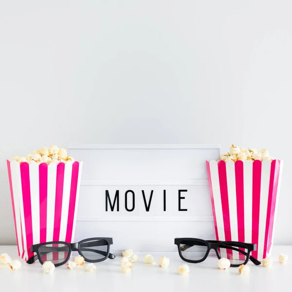 cinema and date concept - two red striped boxes with popcorn, 3d glasses and light box with movie word