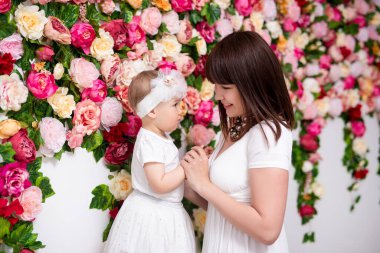 Anneler Günü konsepti. Mutlu, güzel bir anne ve çiçek duvarları arkasında küçük bir kız.