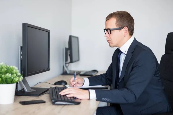 Junger Gutaussehender Geschäftsmann Benutzt Computer Und Schreibt Etwas Auf Klemmbrett — Stockfoto
