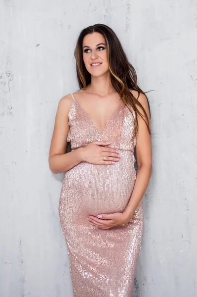 Красивая Беременная Женщина Блестящем Вечернем Платье Позирует Сером Фоне Стены — стоковое фото