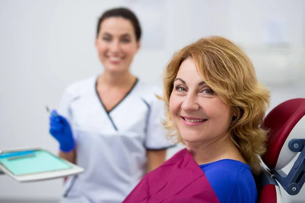 Diş kliniğinde neşeli olgun kadın ve dişçi portresi