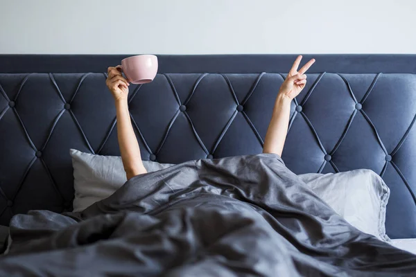 早上好概念 女人的手 手拿着咖啡杯 胜利的标志从卧室的毛毯上伸出来 — 图库照片