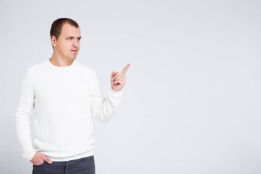 Sıcak kış süveteri giymiş yakışıklı bir adamın portresi gri arka plandaki bir şeyi işaret ediyor.