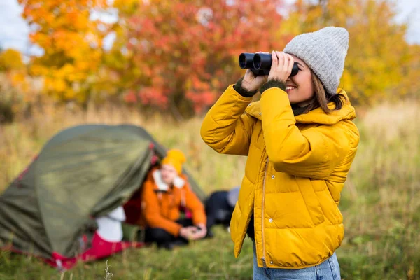 远足及徒步旅行的概念 年轻美丽的微笑女子 戴着双筒望远镜 在秋天的森林中接近绿色帐篷 — 图库照片