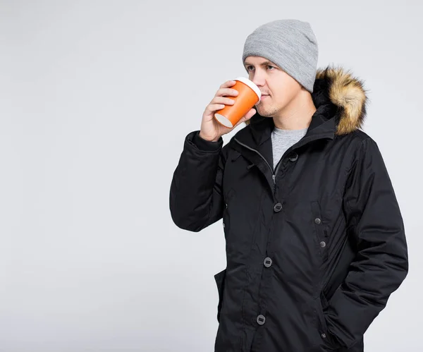 若いですハンサムな男で暖かい冬のジャケット飲料コーヒーや紅茶以上グレーの背景にコピースペース — ストック写真