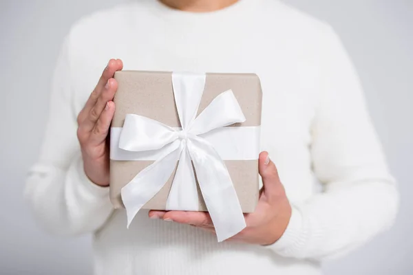 close up of wrapped christmas gift box in male hands over gray background